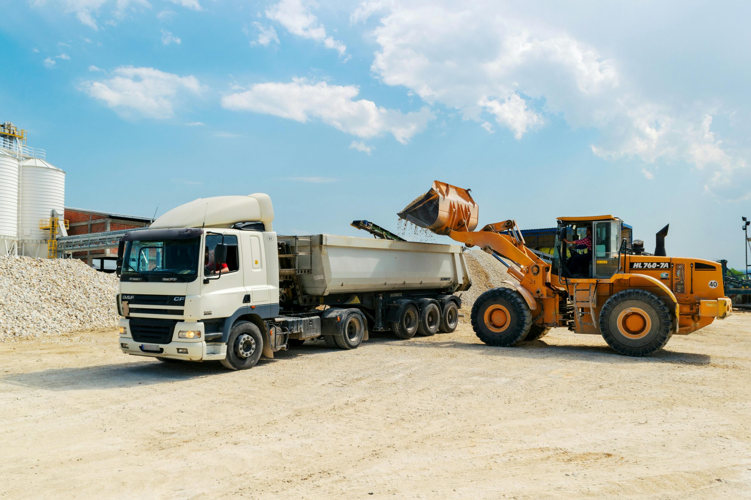 Home Excavator loading materials into a heavy-duty truck at a sunny construction site.