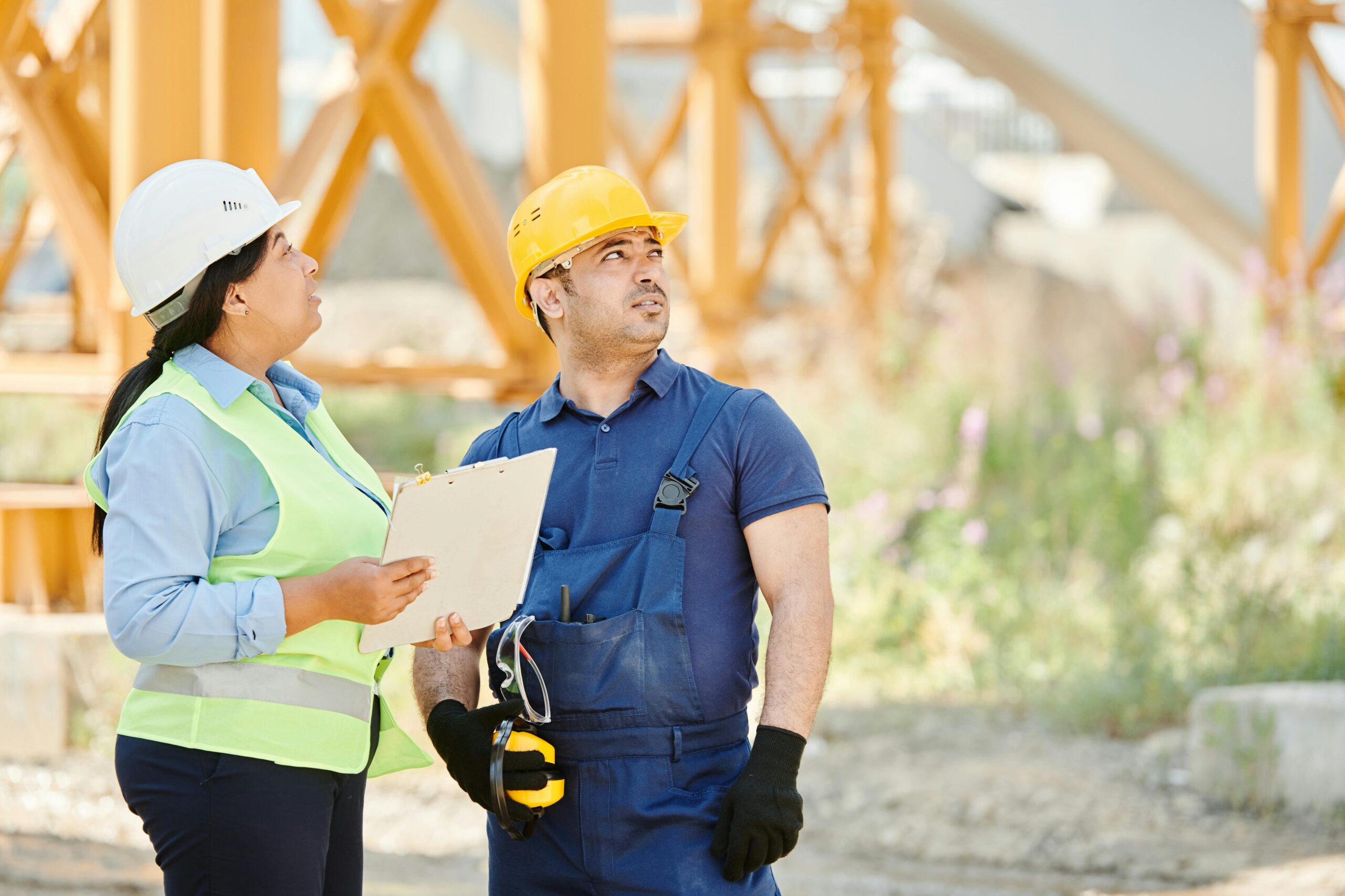 Two construction workers in safety gear discussing site plans at an outdoor construction site.